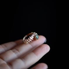 a person is holding a ring with leaves on it and an emerald stone in the middle