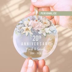 two hands holding a glass ornament with flowers on it and the words 20th anniversary