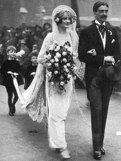 an old black and white photo of a bride and groom walking down the street together