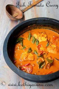 fish tomato curry in a black bowl with a wooden spoon on the table next to it