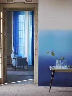 a table with vases and flowers on it in front of a blue painted wall