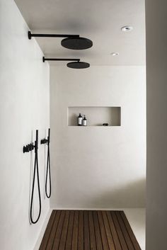 a bathroom with wooden flooring and white walls, two shower heads are on the wall