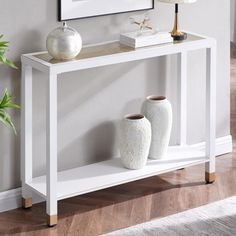 a white console table with two vases on it and a framed photograph above it