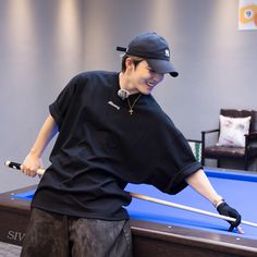 a young man holding a pool cue in his right hand while standing next to a pool table