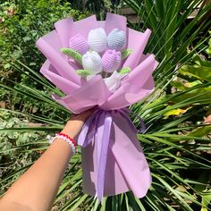 a hand holding a bouquet of crocheted flowers in front of some palm trees