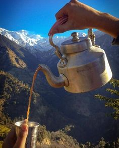 a person pouring tea into a cup with mountains in the background