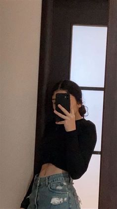 a woman taking a selfie in front of a door with her cell phone up to her face