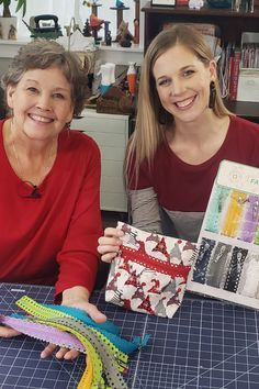 two women are sitting at a table with some sewing supplies in front of them and smiling