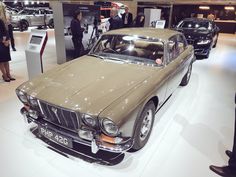 an old car is on display in a showroom while people look at it and talk