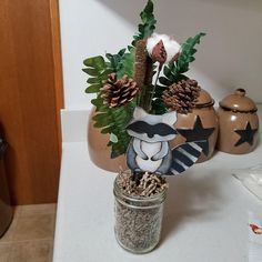 a vase filled with plants and pine cones on top of a counter next to a cookie jar