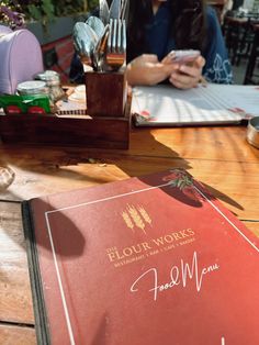 a red book sitting on top of a wooden table next to a fork and knife