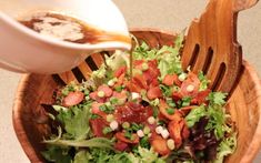 a salad in a wooden bowl being drizzled with dressing on the side