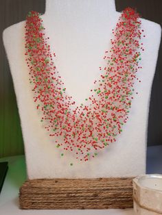 a red and green beaded necklace sitting on top of a white mannequin