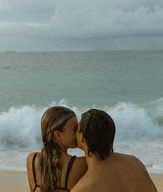 a man and woman kissing on the beach with waves crashing in the backgroud