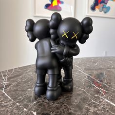 two black figurines are hugging each other on a marble countertop in front of paintings