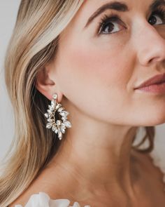 a woman wearing large earrings with flowers on the front and back of her ear, looking off to the side