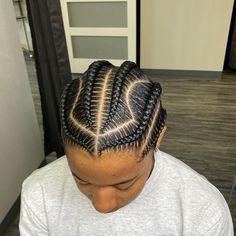 a man with cornrows sitting in front of a hair dryer wearing a gray shirt