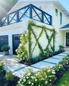 a house with white flowers in front of it and green plants growing on the side