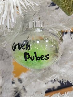 a green ornament hanging from the side of a white christmas tree with words on it