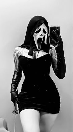 a woman in a black dress and mask taking a selfie with her cell phone