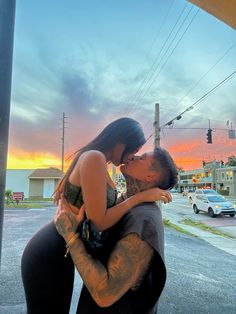 a man and woman kissing in front of a street with the sun setting behind them