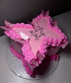 a birthday cake with pink frosting and butterflies on it's side, sitting on a table