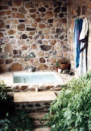 an outdoor hot tub in front of a stone wall and steps leading up to it