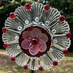 a red glass flower on top of a metal stand in the grass with trees in the background