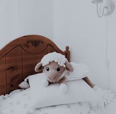 a stuffed sheep laying on top of a bed with white sheets and pillows next to a wooden headboard