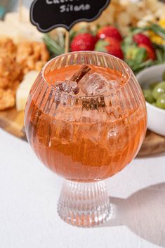 a glass filled with liquid sitting on top of a table next to a bowl of fruit