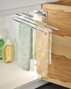 towels hanging on the rail in front of an open cabinet door with soaps and hand sanitizers next to it