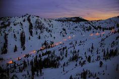 a snowy mountain covered in lots of trees with lights on it's sides at night