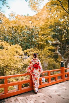 a woman in a kimono standing on a bridge looking at the trees and bushes