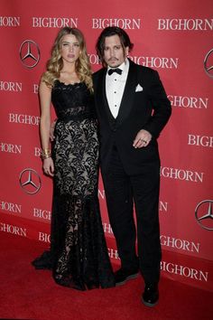 a man and woman standing next to each other in front of a red carpeted wall