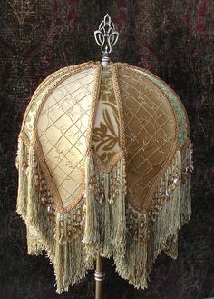 a lamp shade with beaded trim and fringes on a wooden stand in front of a wall