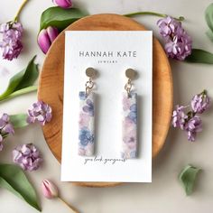 a pair of earrings sitting on top of a card next to some purple and white flowers