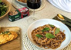 a plate of pasta with basil on top next to some bread and wine glasses, along with other food items