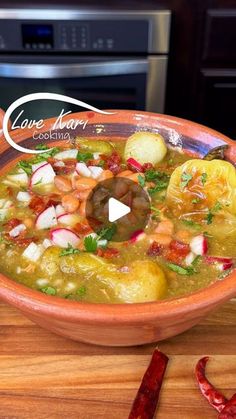 a bowl filled with soup sitting on top of a wooden table next to red peppers