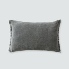 the grey linen pillow with fringe trims is shown in front of a white background