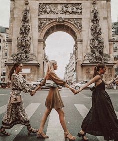 three women are crossing the street in front of an arch