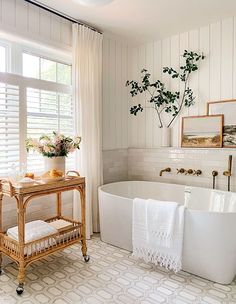 a white bath tub sitting under a window next to a wooden table with towels on it