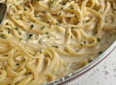 a bowl filled with pasta and sauce on top of a white countertop next to a silver spoon