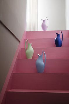 three different colored vases sitting on top of pink steps in front of a window