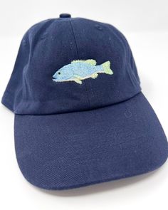 a blue hat with a fish embroidered on the front and side, sitting on a white surface