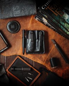 an assortment of personal items laid out on top of a wooden table, including pens and notebooks