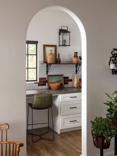 an archway leads into a kitchen with white cabinets and counter tops, along with potted plants