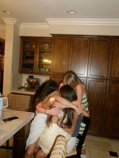 a group of young women hugging each other in a kitchen with wooden cabinets and counter tops