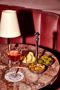 a table topped with a glass of wine next to a plate of chips and olives