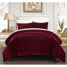 a bed covered in a maroon comforter and pillows