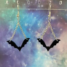 two bats dangling from chains in front of a colorful background with stars and space behind them